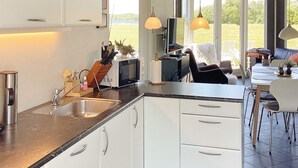 A modern kitchen with white cabinets, a black countertop, and a dining area with a table and chairs. - 4 Star Holiday Home in Ansager (Ansager)