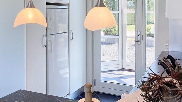 Una cocina con dos lámparas colgantes, un refrigerador y una puerta que da al exterior.