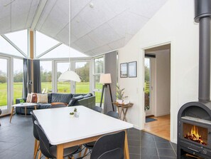 A modern living room with a fireplace, a dining area, and large windows offering a view of the outdoors.