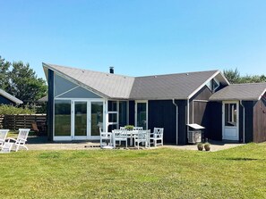 A modern house with a large glass door, a patio with outdoor furniture, and a well-maintained lawn.