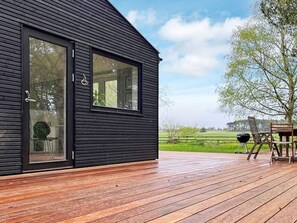 A modern building with a large glass door and windows, a wooden deck, and outdoor furniture. - 6 Person Holiday Home in Gilleleje (Gilleleje)