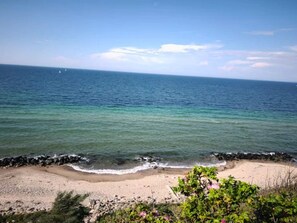 A beach with clear water, a rocky shoreline, and vegetation in the foreground.