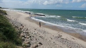 Ein Strand mit felsigem Ufer, Wellen schlagen ans Land, und ein klarer Himmel.