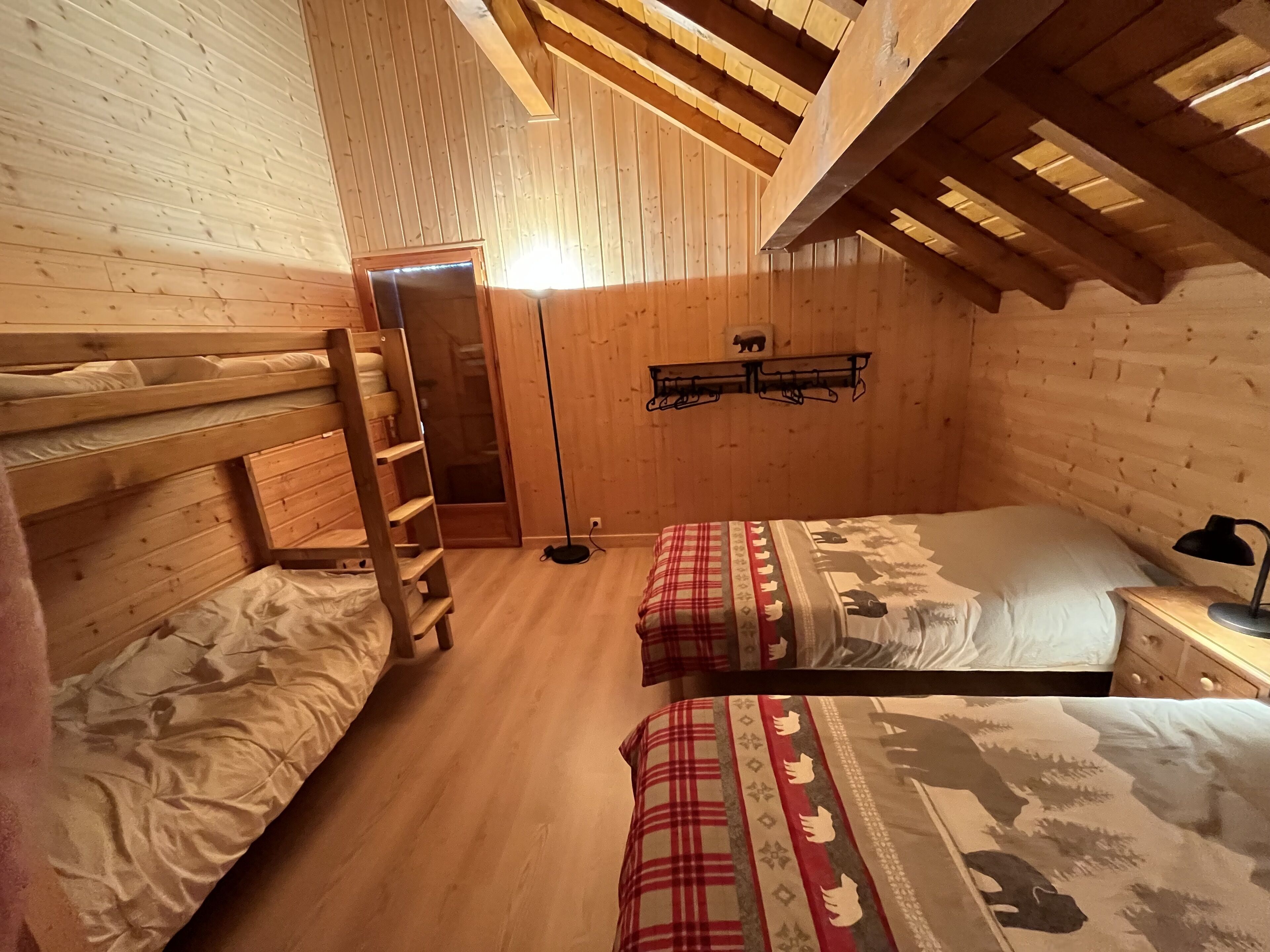 Camera da letto in una baita di legno con letti a castello, un comodino, una lampada e un appendiabiti a parete.