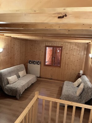 Una habitación acogedora con paneles de madera, un sofá, una silla, una mesita y un ventanal.