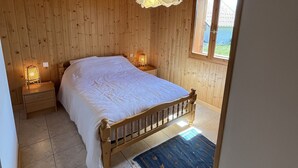 A wooden-paneled bedroom with a bed, nightstands, a hanging light fixture, and a view through a window. - Chalet + sauna with panoramic views in beautiful surroundings (Albiez-le-Jeune)