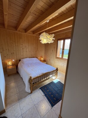 Un dormitorio con paneles de madera, una cama, mesitas de noche, una lámpara colgante y vistas por una ventana.