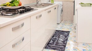 A modern kitchen with white cabinets, a stainless steel stove, a washing machine, and a window with a view of greenery. - Luigi's room Sorrento (Meta)