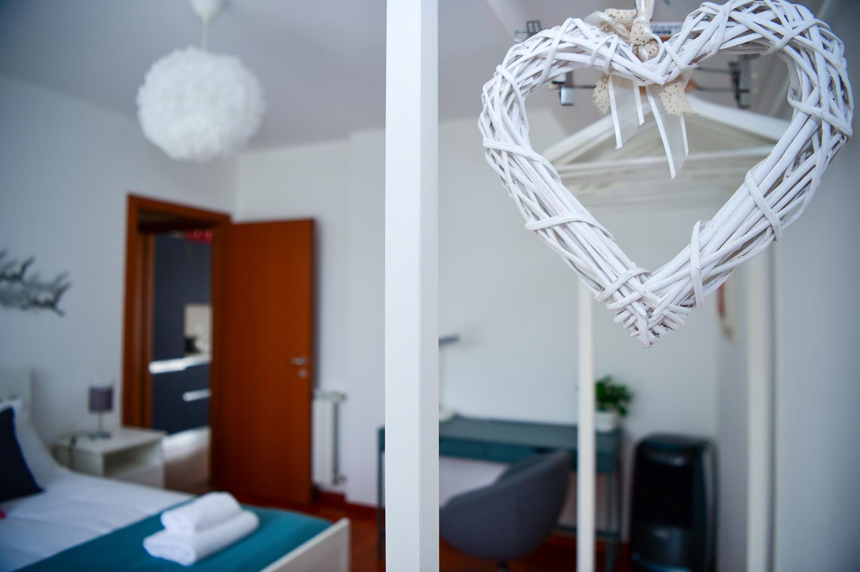 A hotel room with a bed, bedside table, and a hanging heart-shaped decoration.