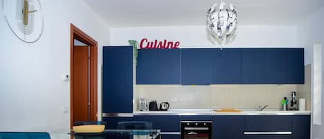 Une cuisine moderne avec des meubles bleu foncé, un plan de travail blanc et un coin repas comprenant une table et des chaises en verre.