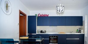 A modern kitchen with dark blue cabinets, a white countertop, and a dining area with a glass table and chairs. - Blue Bellagio by Wonderful Italy (Bellagio)