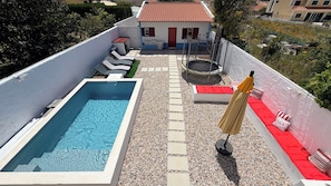 Un espace piscine aménagé sur le toit, avec une piscine rectangulaire, des chaises longues et un petit bâtiment doté d’un toit recouvert de tuiles rouges.