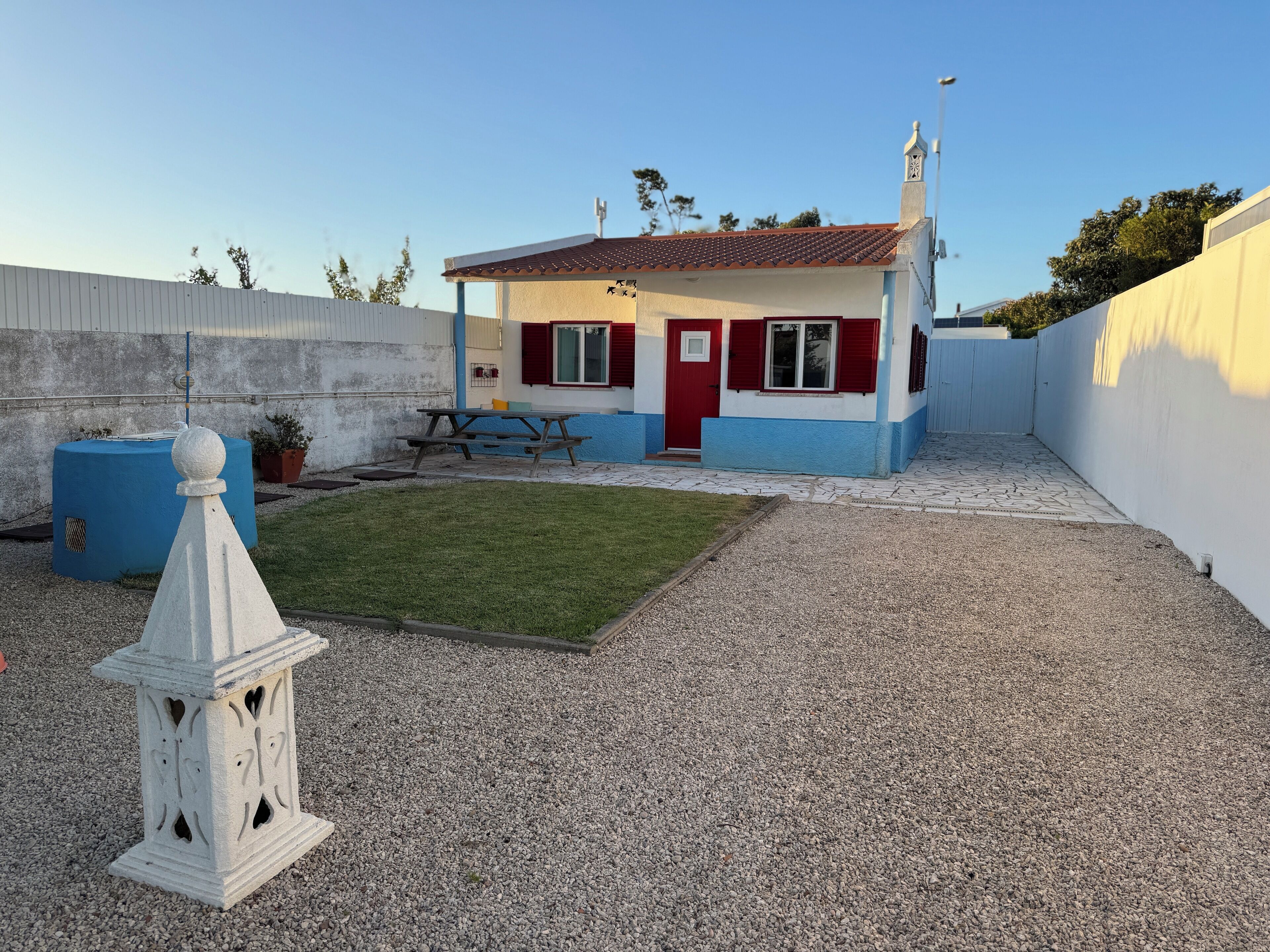 A small house with a red door, a blue and white exterior, and a gravel yard.