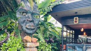 A building with a large glass entrance, surrounded by lush greenery and a decorative sculpture. - 24 On Basil Boutique Luxury Hotel (Randburg)