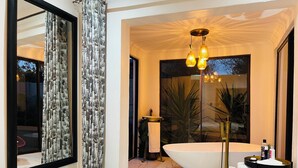A modern bathroom with a freestanding bathtub, a large mirror, and a chandelier. - 24 On Basil Boutique Luxury Hotel (Randburg)