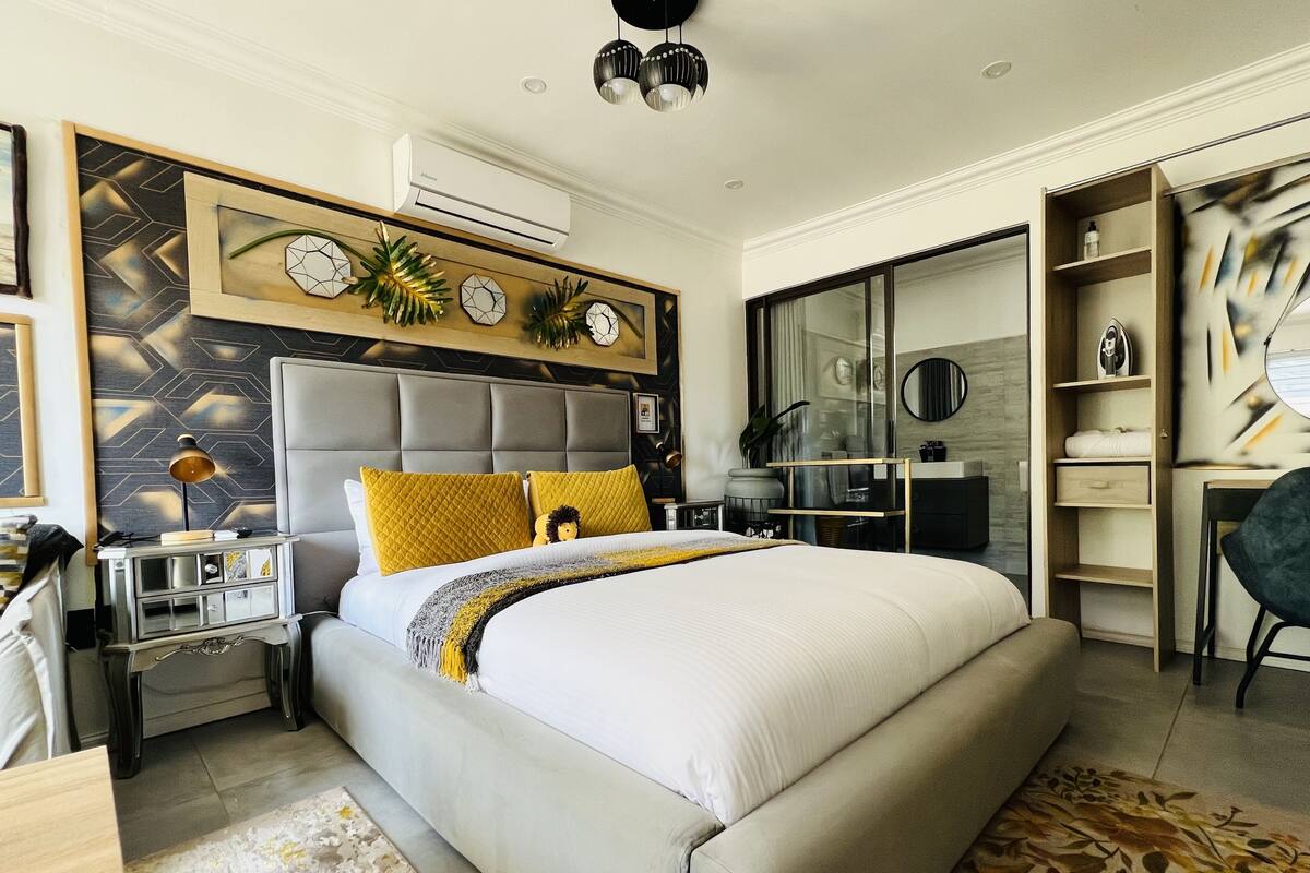 A modern bedroom with a large bed, a nightstand, a dresser, and a built-in wardrobe.