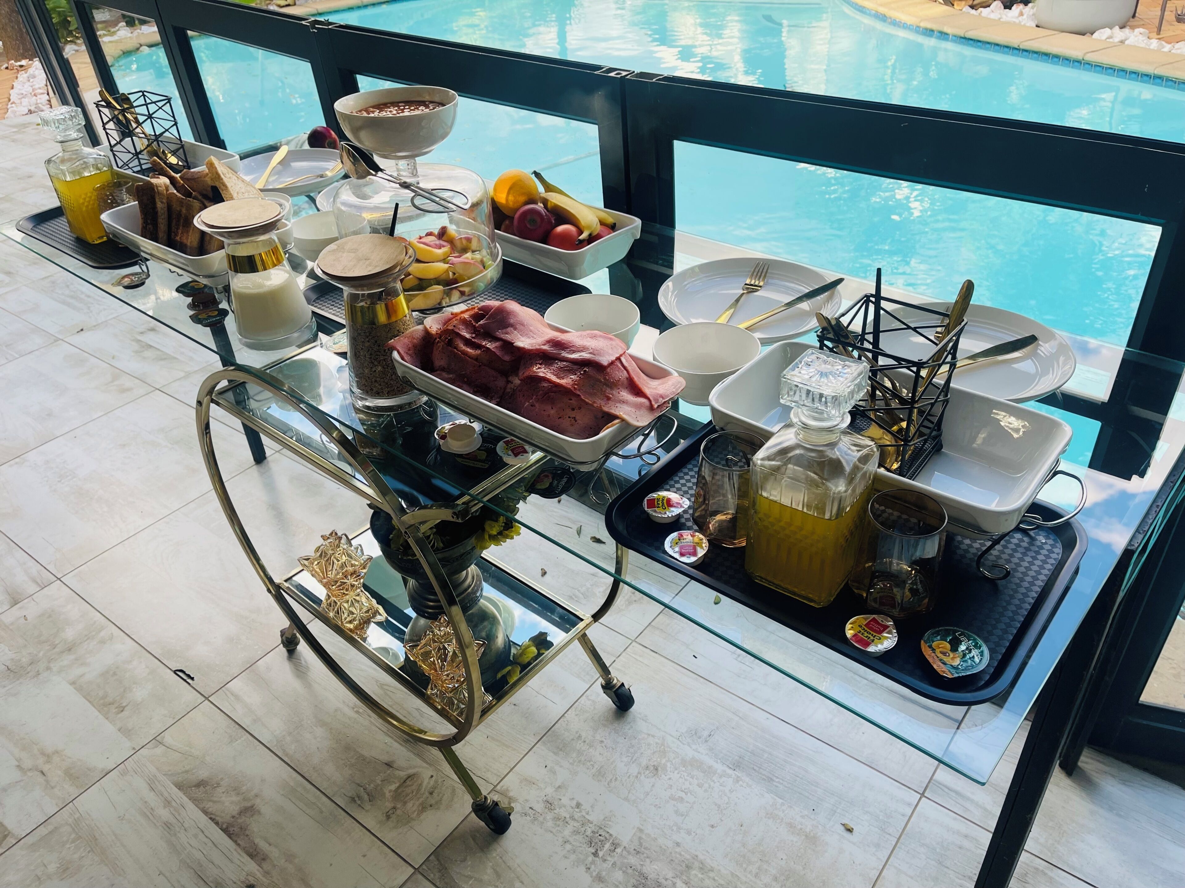 A breakfast trolley with various food items and condiments by a poolside.
