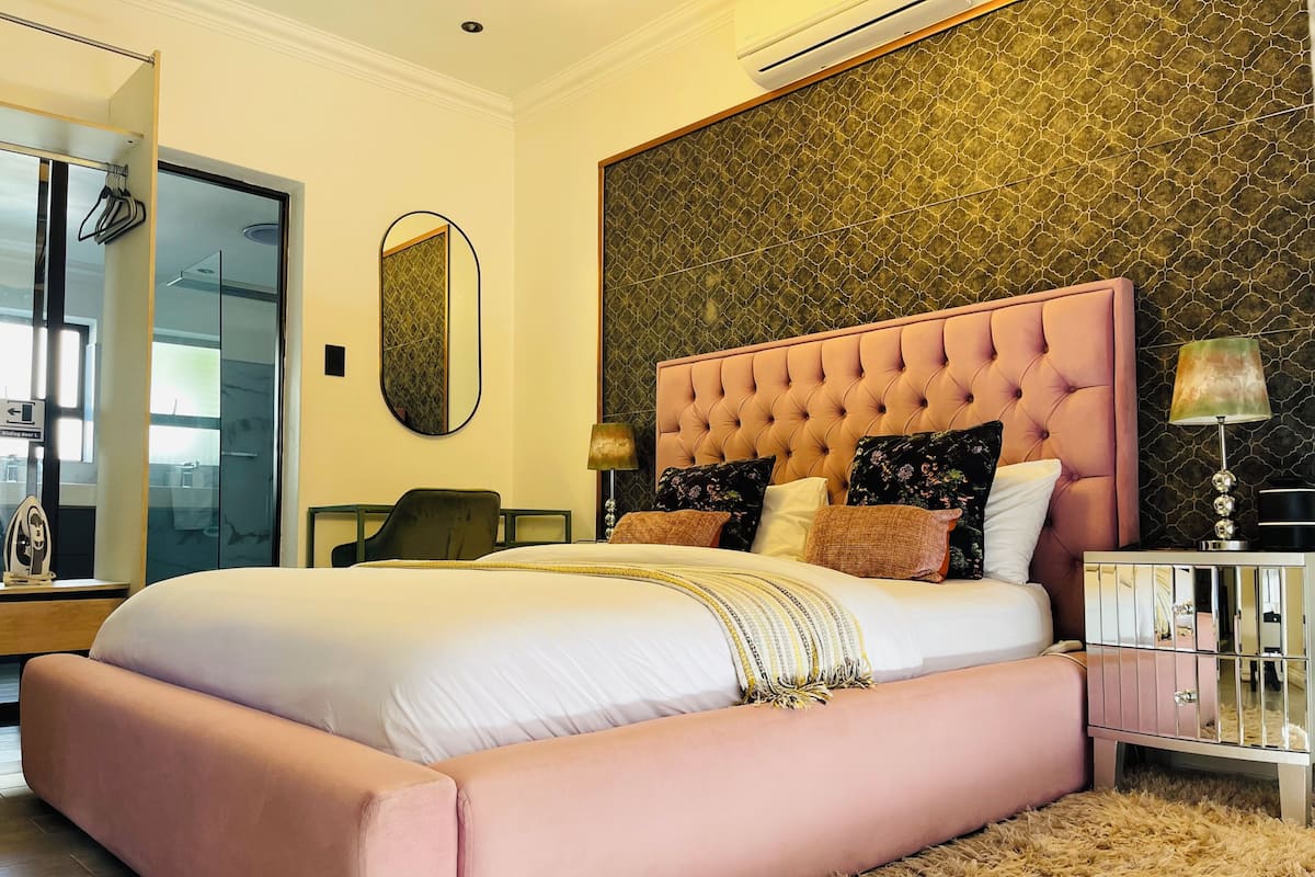 A bedroom with a large bed, a mirror, a nightstand, and a lamp.