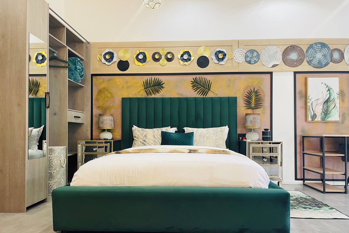 A modern bedroom with a large bed, a green upholstered headboard, and a wall decorated with circular patterns.