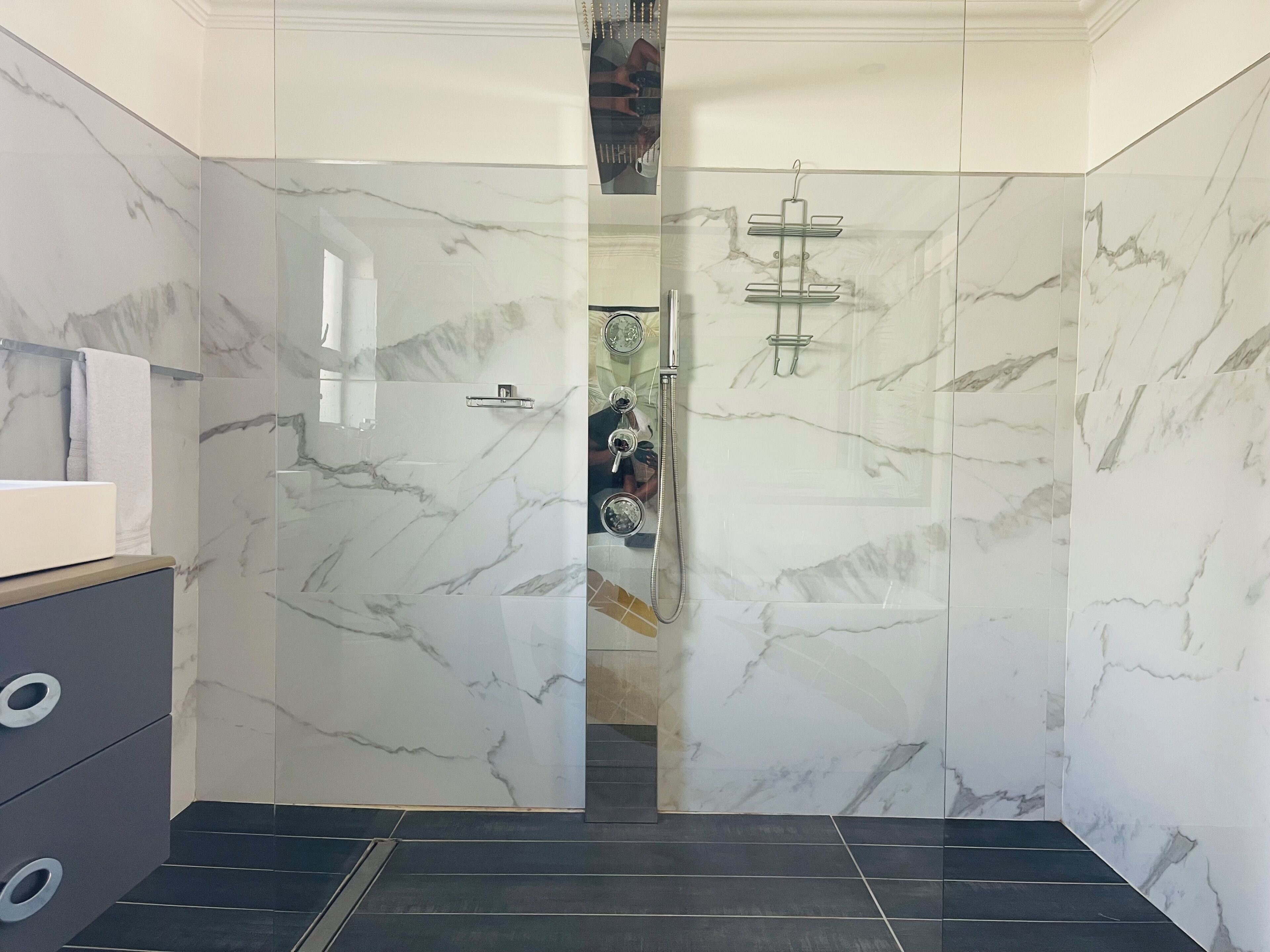 A modern bathroom with marble walls, a glass shower enclosure, and a black tiled floor.