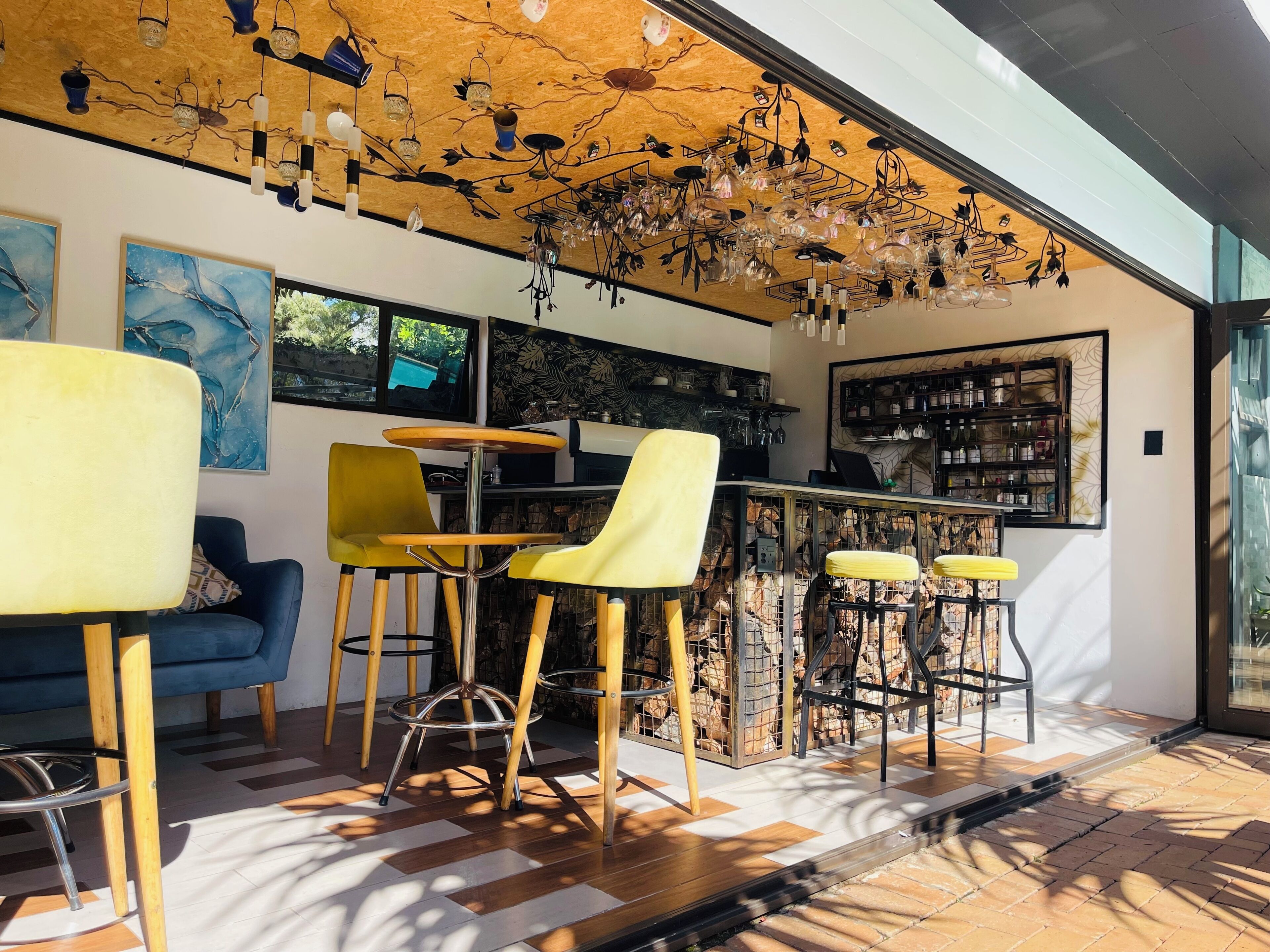 A modern bar area with wooden stools, a blue sofa, and a ceiling with hanging light fixtures.