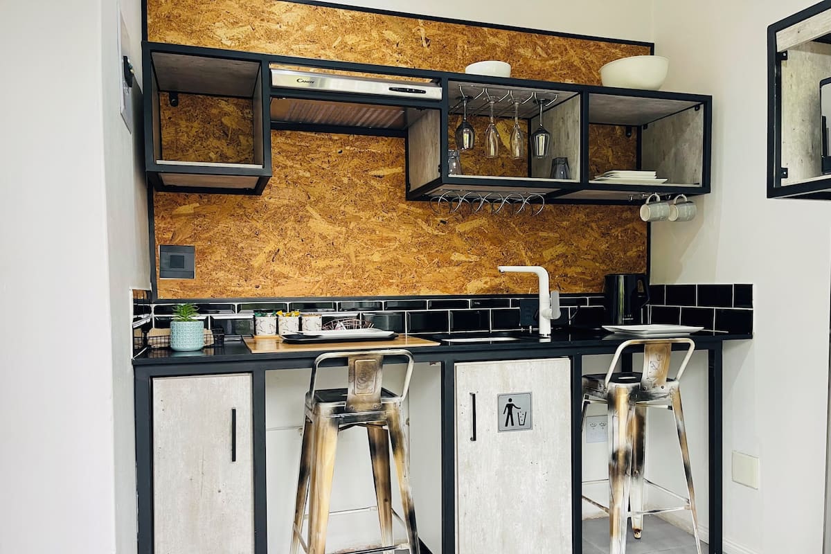 A kitchen with a wooden backsplash, black countertops, and a built-in stove. There are two bar stools and a small sink.