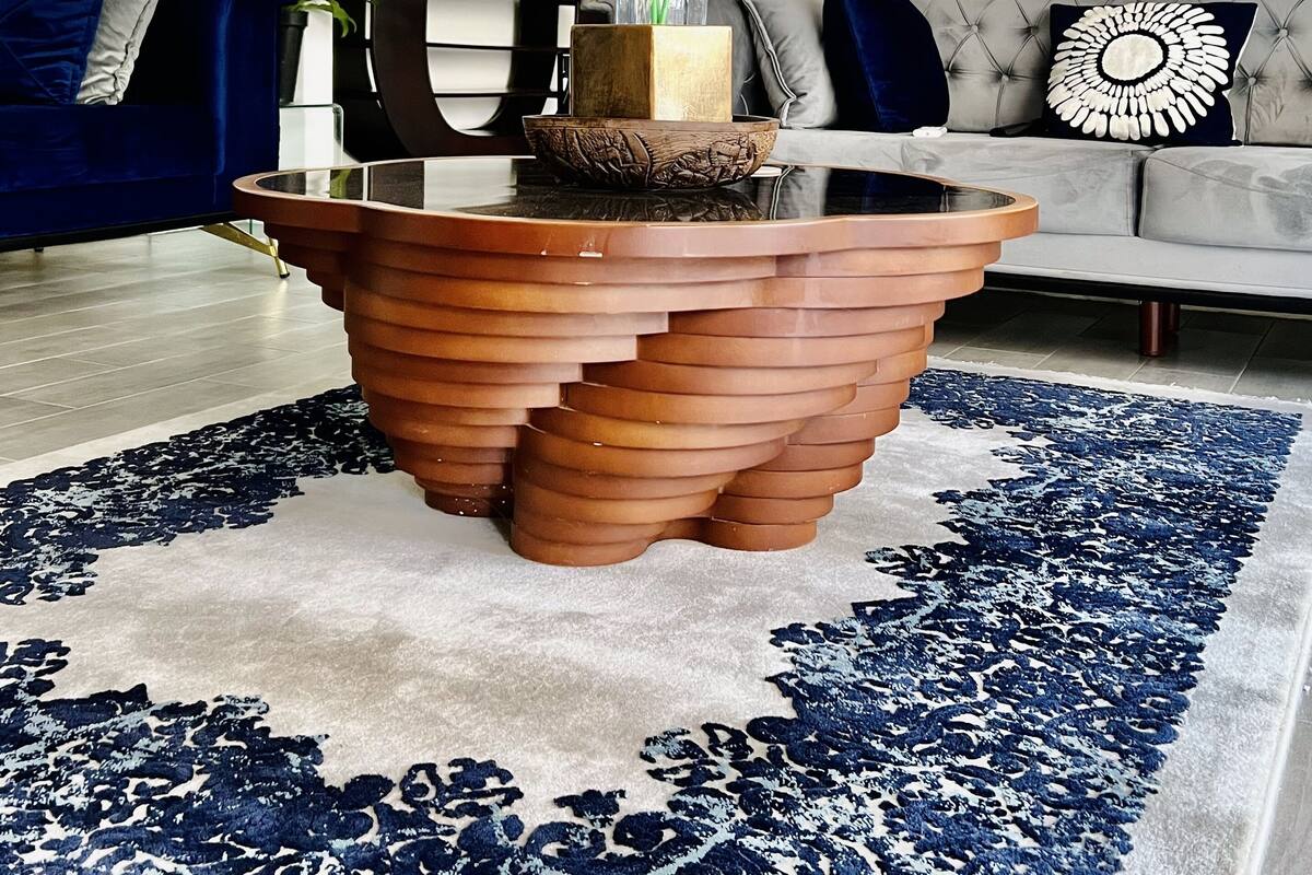 A modern living room with a unique terracotta coffee table, a blue patterned rug, and a grey sofa with decorative pillows.