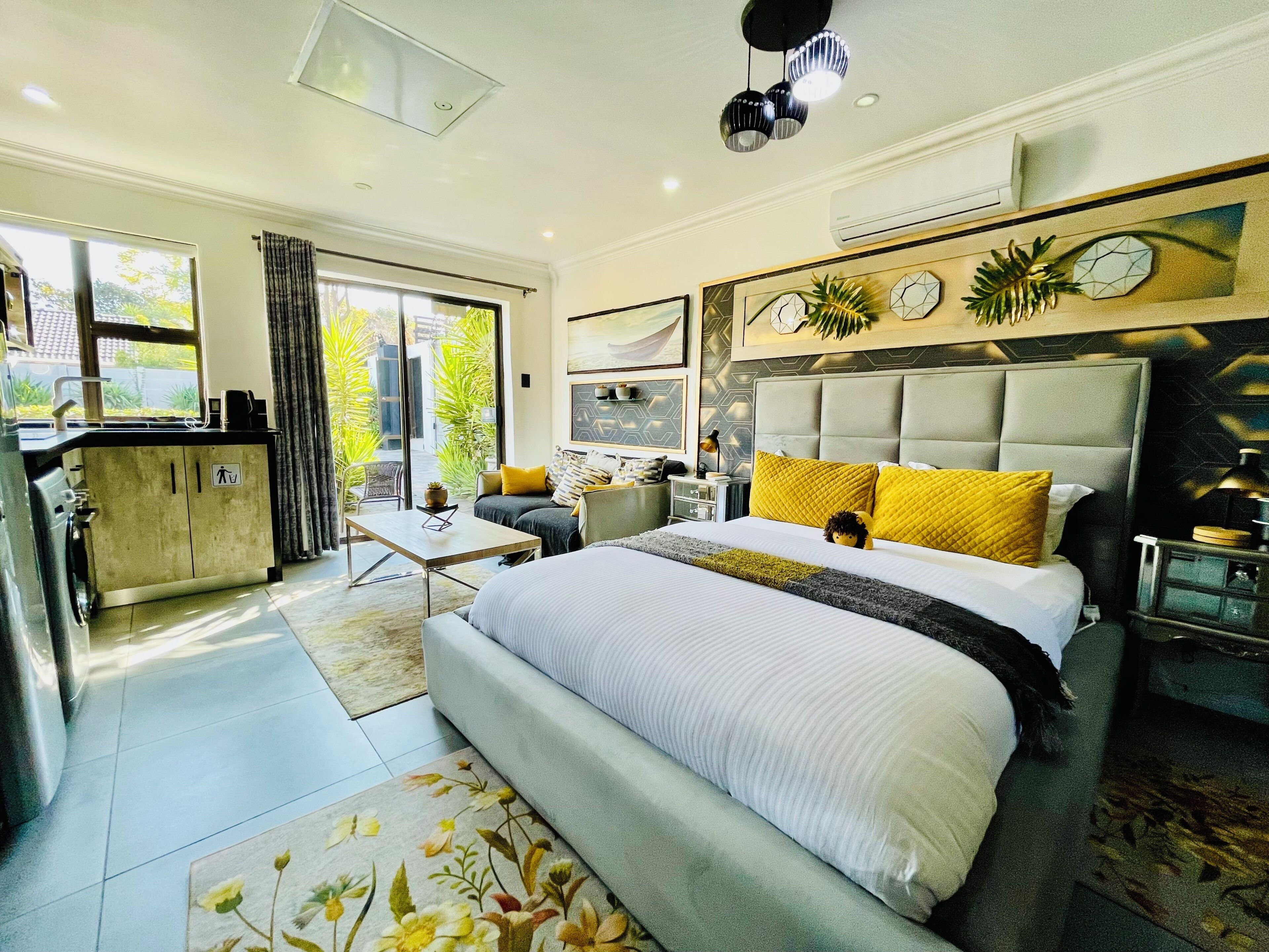 A modern bedroom with a large bed, a sofa, a dining table, and a kitchen area.