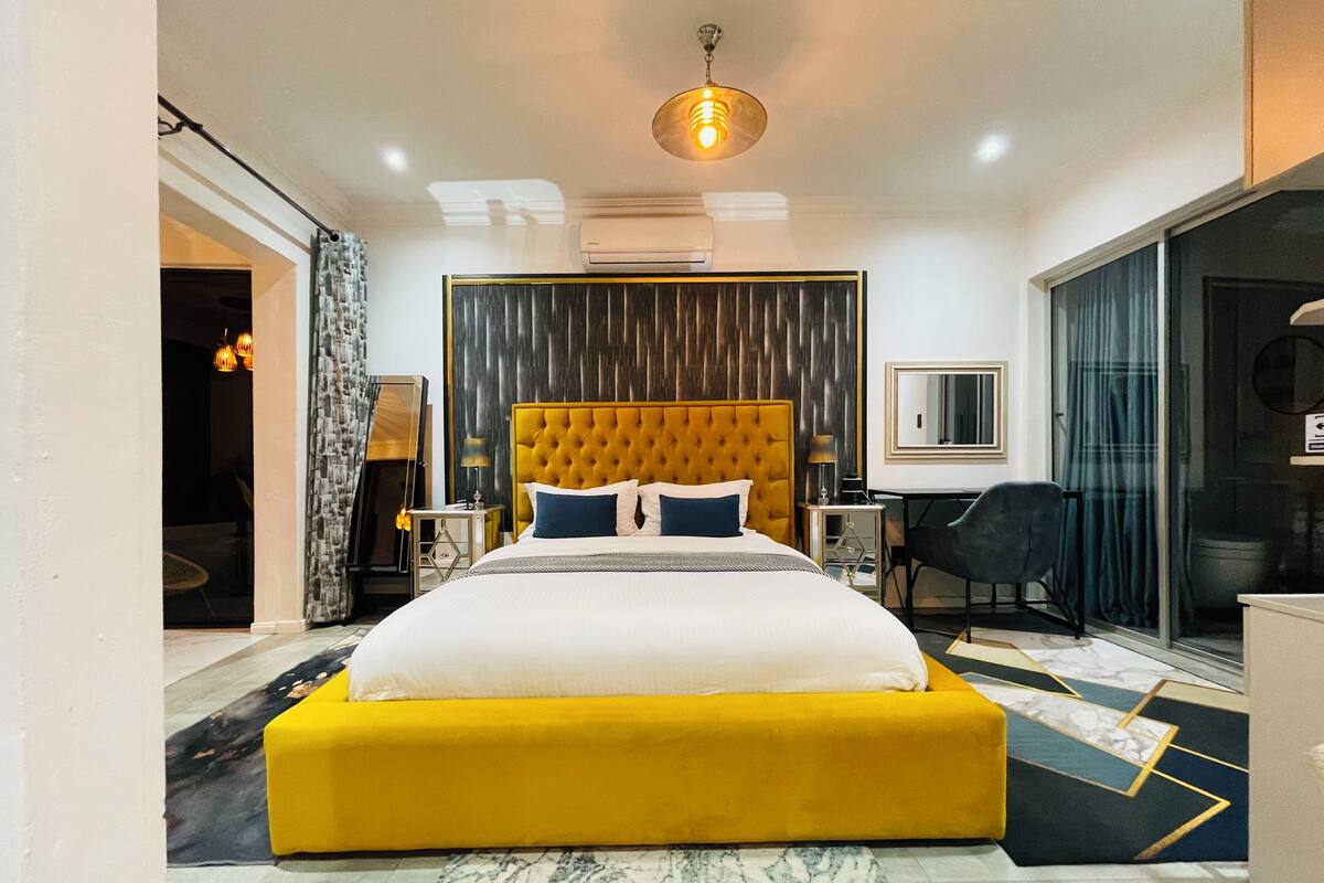 A modern hotel room with a large bed, a desk, a chair, and a large window.