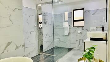 A modern bathroom with a glass-enclosed shower, marble tiles, a white sink, and a small plant on a round table.
