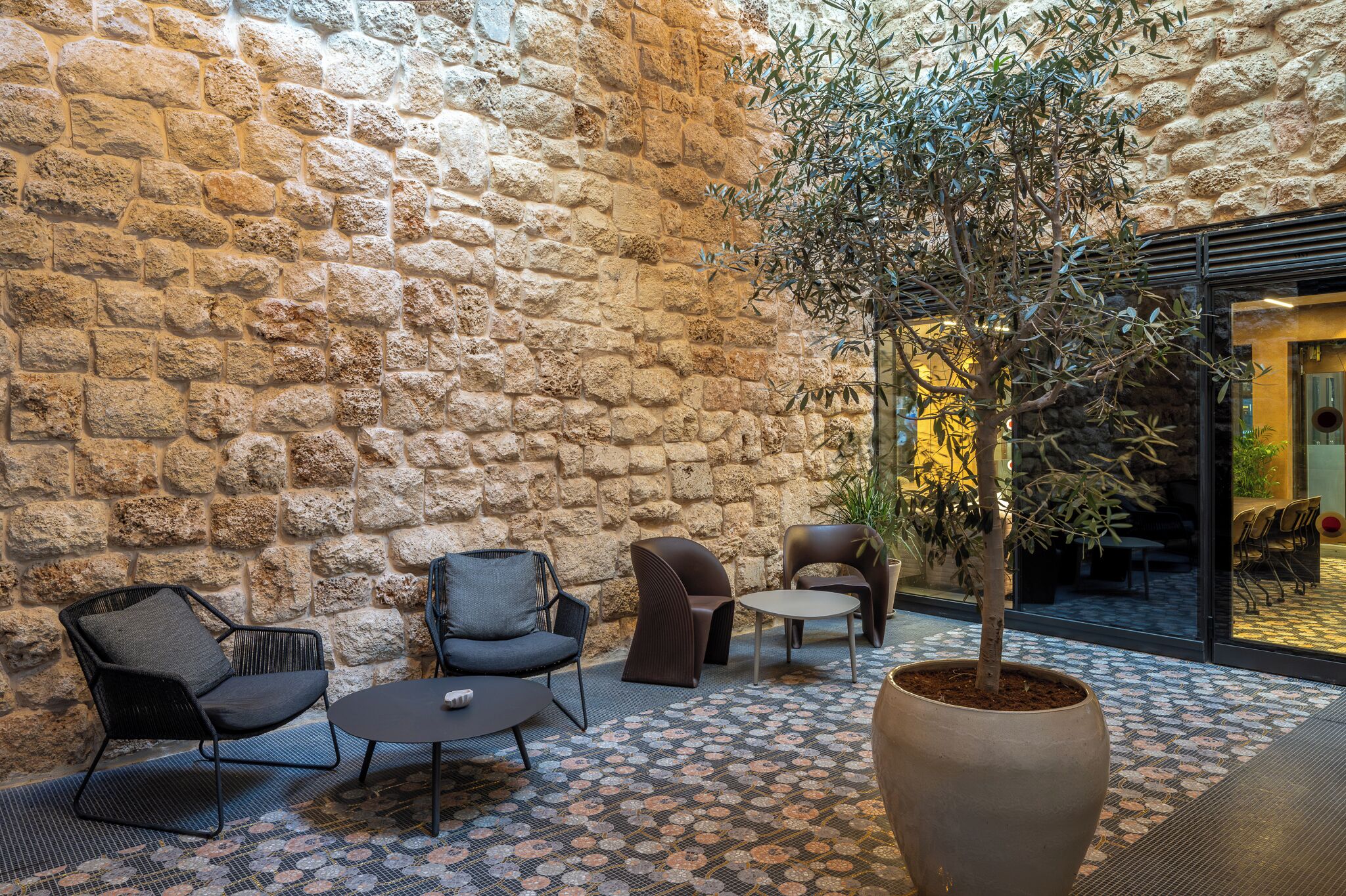 A stone-walled indoor patio with modern furniture and a potted tree.