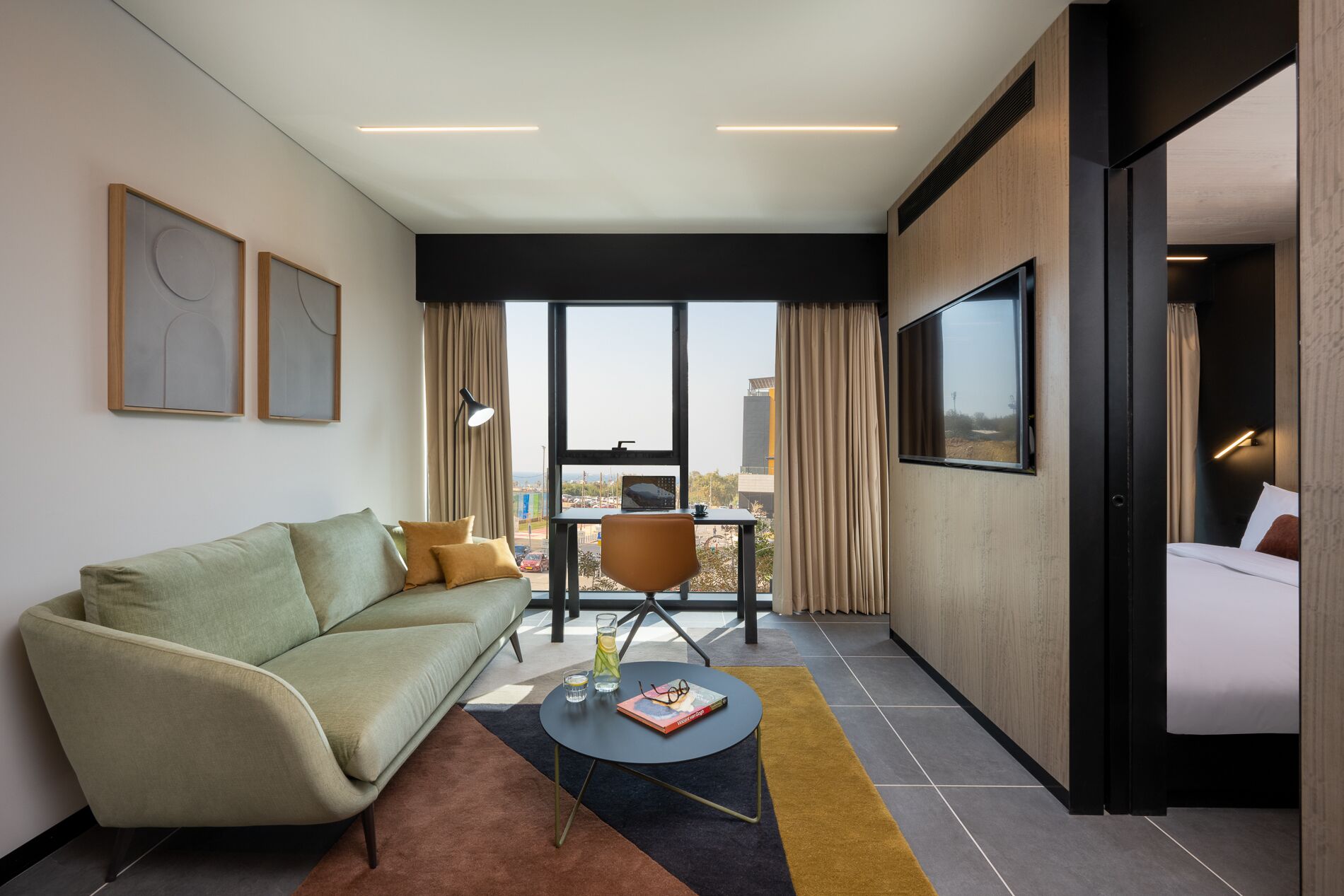 Una habitación de hotel moderna con un sofá, una mesita redonda pequeña, una silla y una cama.