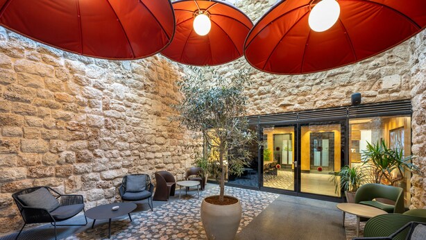 Un área de estar interior acogedora con paredes de piedra, mobiliario moderno y sombrillas rojas que dan sombra.