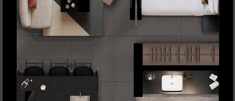 A modern hotel room with a bed, a sofa, a desk with a laptop, a small table with a book, a bathroom with a sink, toilet, and shower.
