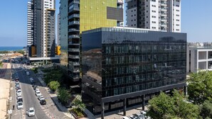 Un edificio moderno con fachada de vidrio, rodeado de rascacielos y una calle concurrida.