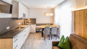 Et kompakt køkken med spiseplads, en sofa med en grøn pude og en trædør.