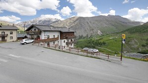 A building with a balcony, a parking area, and a mountainous backdrop. - Studio Apartment "Trela" near Slopes with Balcony & Wi-Fi (Livigno)