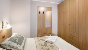 A bedroom with a bed, a wooden wardrobe, a nightstand with a lamp, and a mirror. - Studio Apartment "Trela" near Slopes with Balcony & Wi-Fi (Livigno)