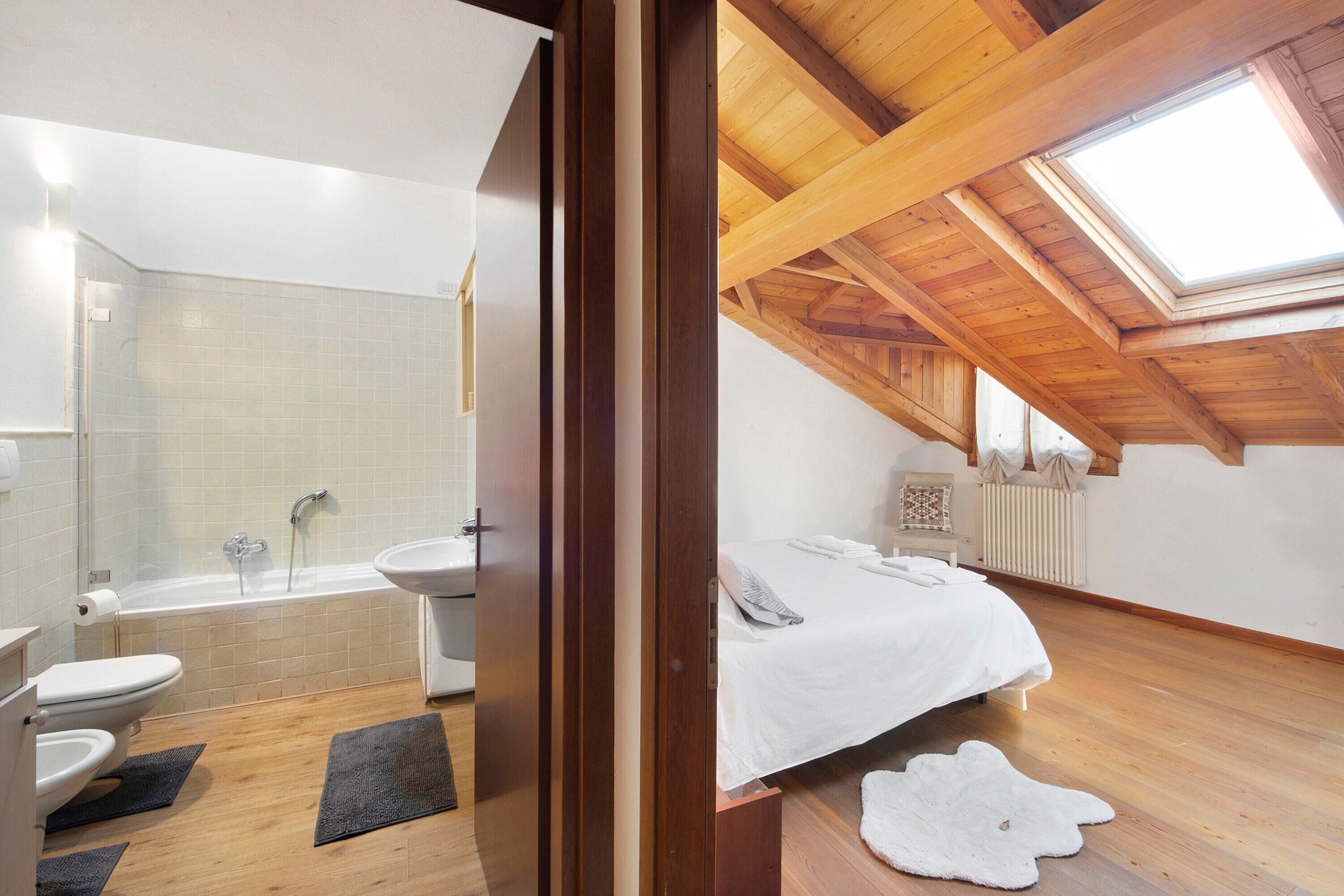 Ein Schlafzimmer mit Oberlicht, einem Bett, einer Heizung und einem Badezimmer mit Badewanne und Toilette.