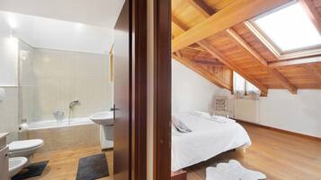 Ein Schlafzimmer mit Oberlicht, einem Bett, einer Heizung und einem Badezimmer mit Badewanne und Toilette.