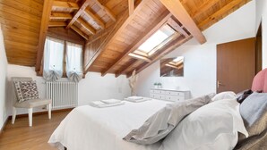 Un dormitorio con techo inclinado, una cama, una silla, un aparador y un radiador.