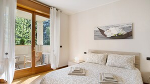 A bedroom with a bed, a nightstand, a lamp, a window with curtains, and a painting on the wall. - Apartment 'Casa Rosada Monza Autodromo' with Balcony, Wi-Fi and Air Conditioning (nova milanese)