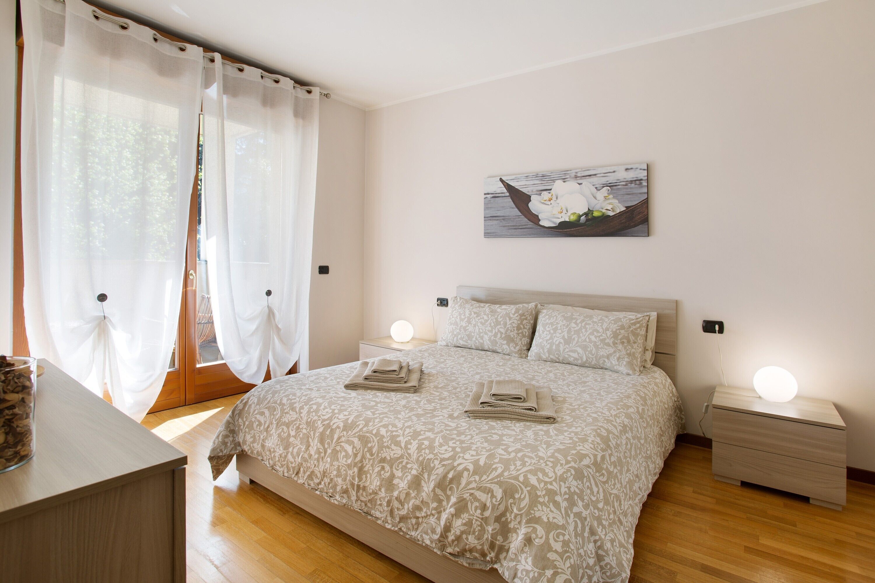 A bedroom with a bed, bedside tables, a nightstand, a lamp, and a window with curtains.