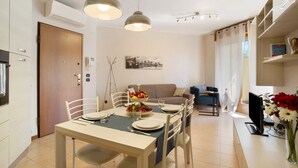 A dining area with a table set for four, a sofa, and a TV in a modern living space. - Apartment 'Casa Rosada Monza Autodromo' with Balcony, Wi-Fi and Air Conditioning (nova milanese)