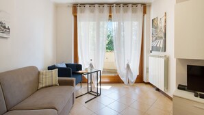 A living room with a sofa, a small table, a TV, and a window with curtains. - Apartment 'Casa Rosada Monza Autodromo' with Balcony, Wi-Fi and Air Conditioning (nova milanese)