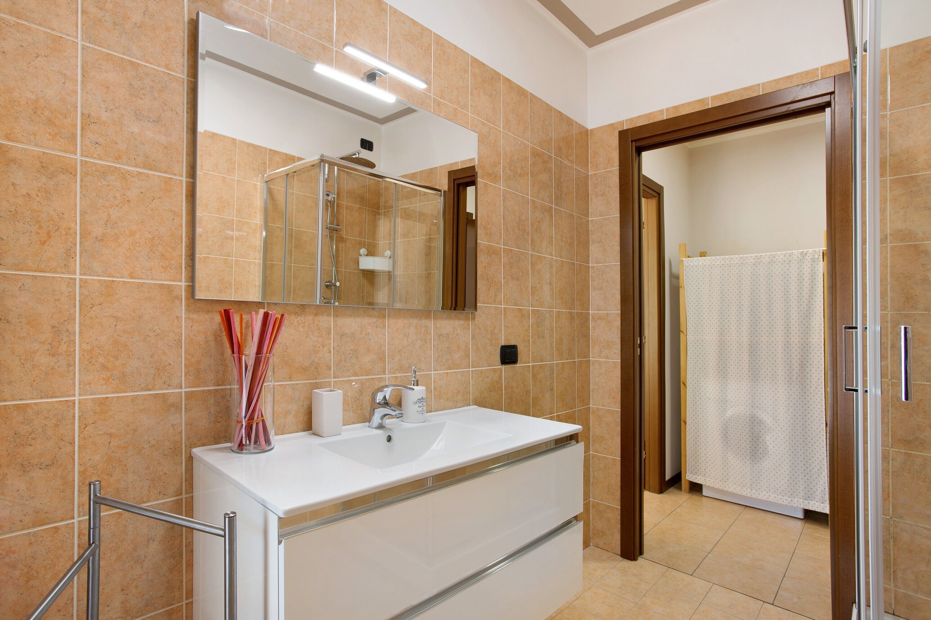 A bathroom with a large mirror, a sink, a shower, and a toilet.