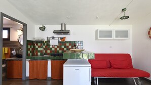 Eine kompakte Küche mit Kühlschrank, Spüle und Herd. Es gibt ein rotes Sofa und einen kleinen Esstisch.