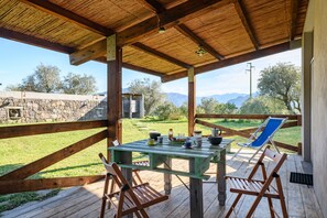 A covered outdoor area with a table and chairs, a view of the landscape, and a stone wall. - Studio Apartment "Naramanue 2" with Mountain View, Private Terrace & Wi-Fi (Dorgali)