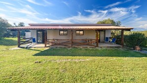 Una casa de un piso con techo de tejas, un porche cubierto con mobiliario y un patio con césped.