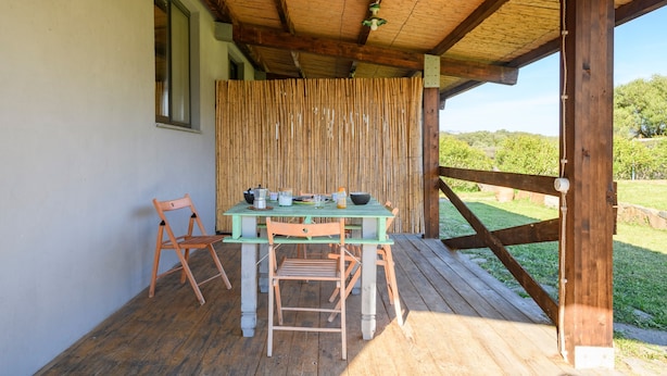 Un espacio de comedor al aire libre techado con mesa y sillas, una ventana y vistas del paisaje.